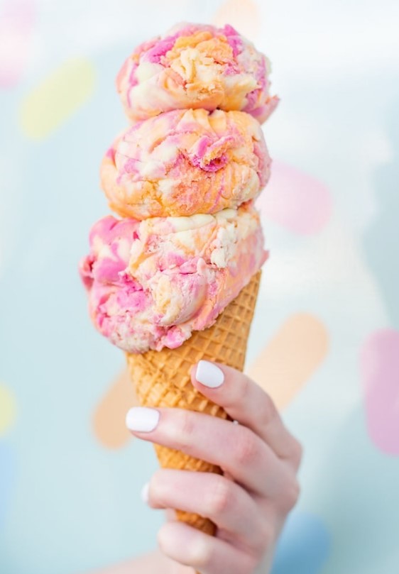 Hand holding a three-scoop ice cream cone.